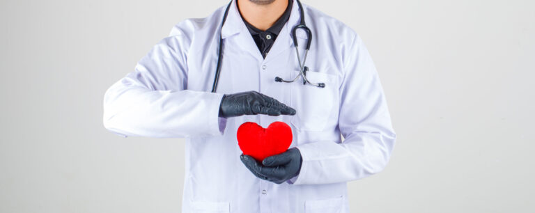 Doctor holding heart in white coat with stethoscope and looking positive , front view